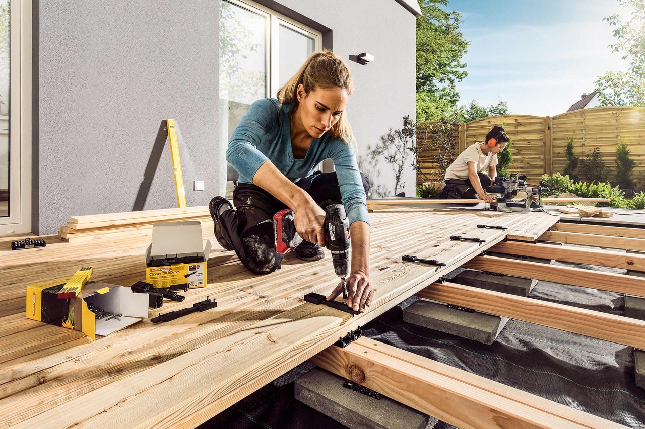 Două persoane montează o terasă din lemn cu o șurubelniță fără fir și cleme pentru terasă.
