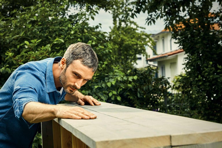 Bărbat inspectând o construcție din lemn în grădină