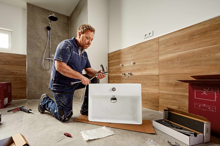 Un instalator montează o chiuvetă într-o baie cu duș.