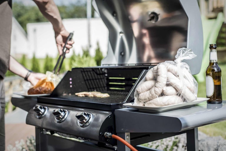 Scenă de grătar cu grătar, cârnați și o persoană cu clești de grătar