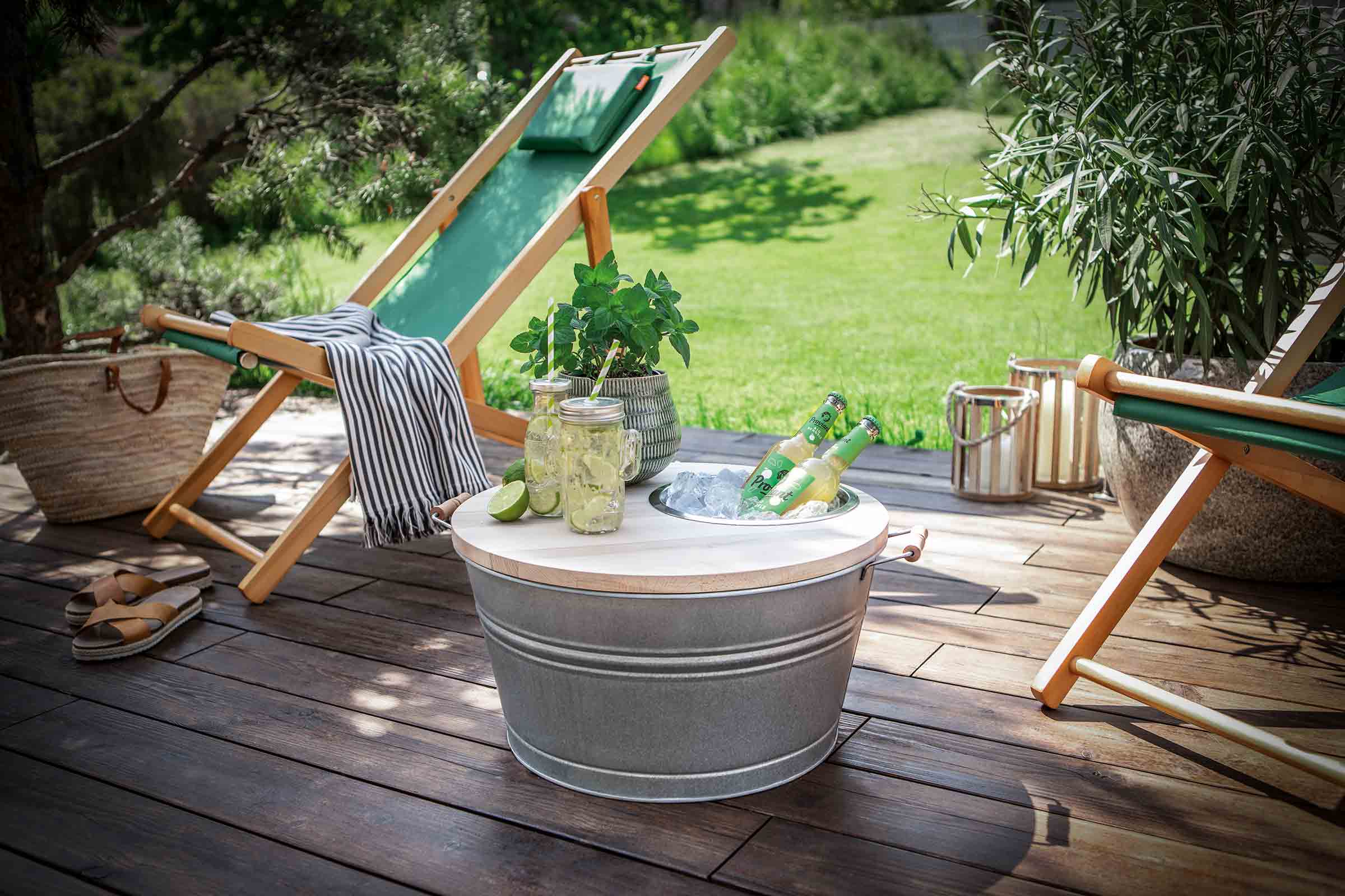 Scenă de grădină estivală cu șezlonguri, răcitor de băuturi cu gheață și băuturi, pahare cu limonadă, plante și decorațiuni pe o terasă din lemn