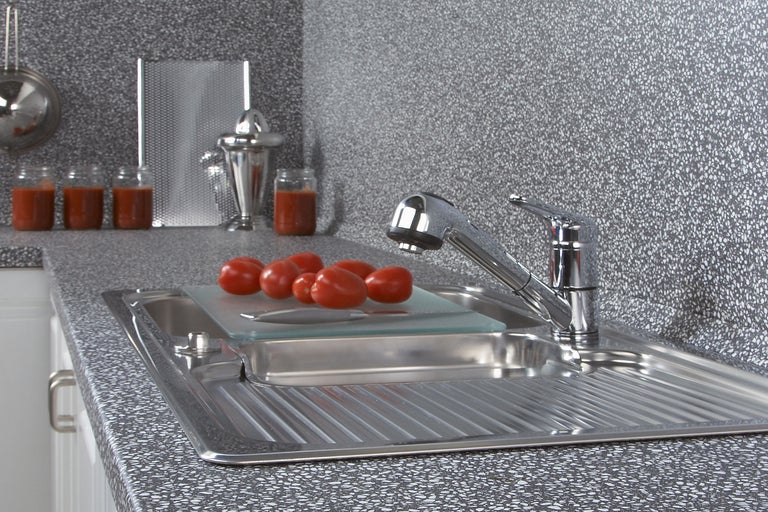 Scenă de bucătărie cu chiuvetă, robinet, tocător și roșii pe un blat de lucru