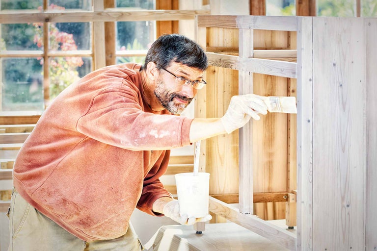 Un bărbat vopsește un dulap de lemn cu o pensulă.