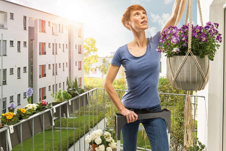 Femeie care decorează balconul cu un ghiveci suspendat și jardiniere.