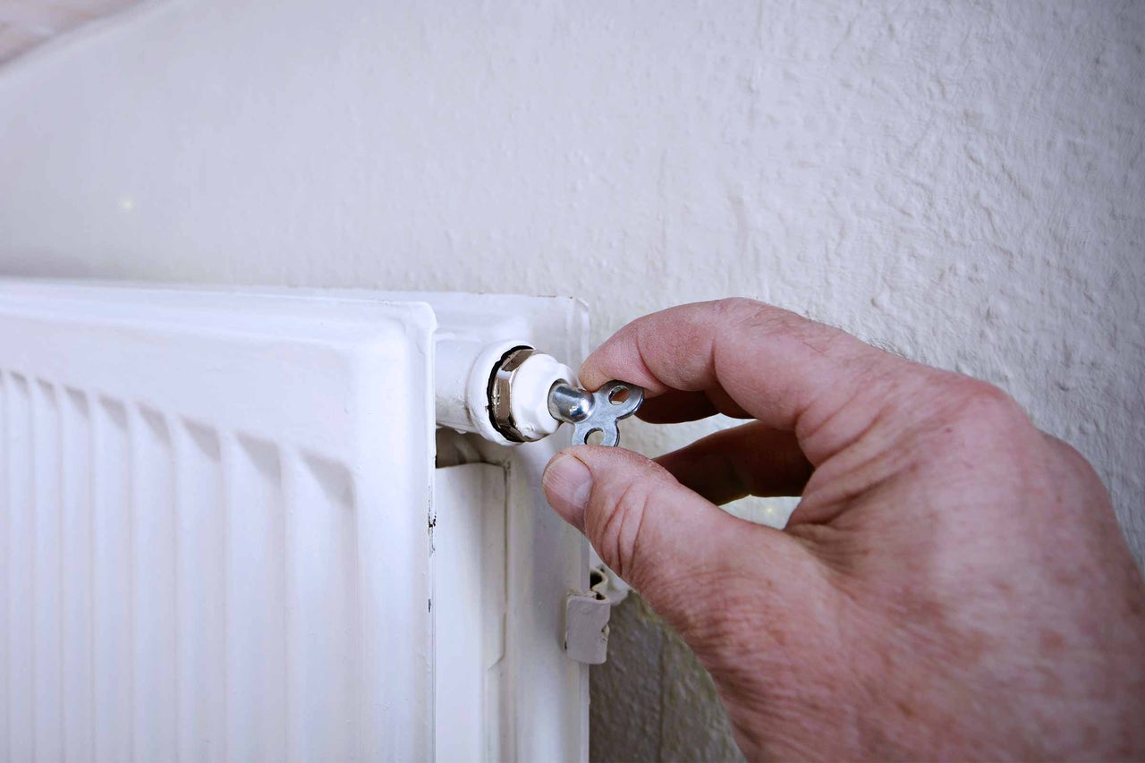 Mână acționând o cheie de aerisire pe un radiator