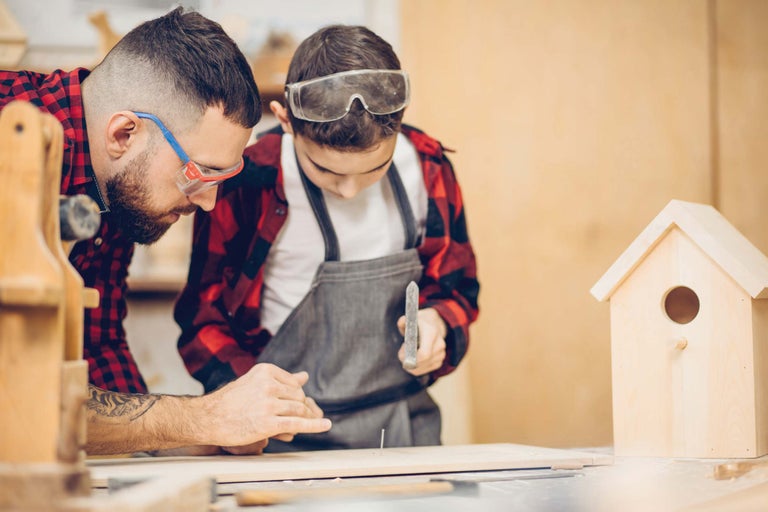 Tată și fiu construiesc împreună o casă de păsări cu ciocanul și cuiul.