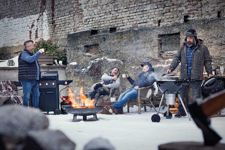 Grup de bărbați fac grătar iarna afară cu grătar pe gaz, grătar pe cărbune și vatră.