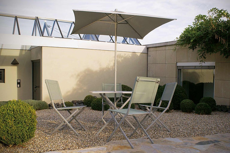 Scenă de grădină cu masă de grădină, scaune de grădină și umbrelă de soare pe un teren pietruit