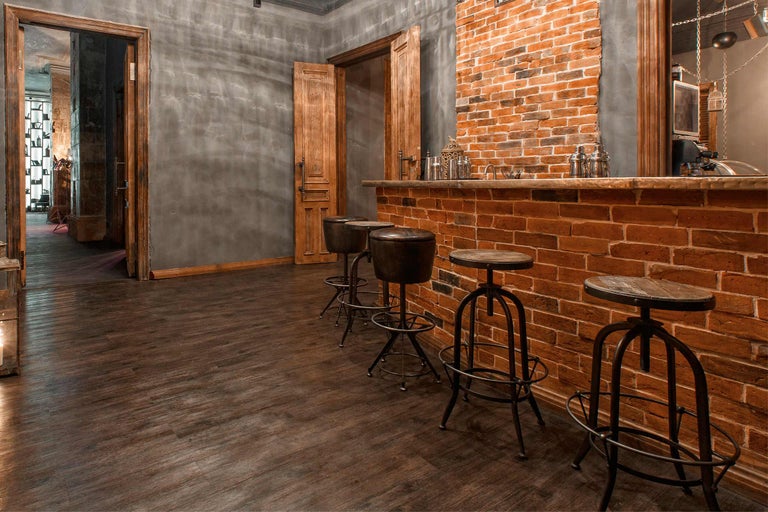 Bar cu tejghea din cărămidă și scaune de bar într-o cameră cu podea din lemn