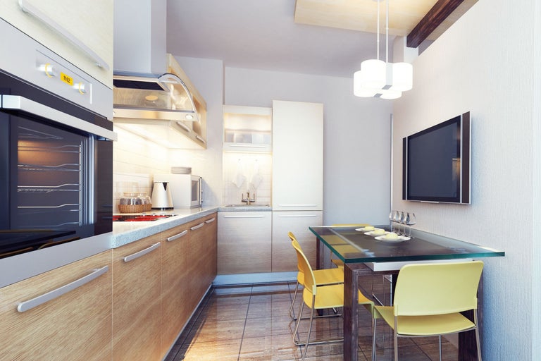 Bucătărie luminoasă cu fronturi din lemn, masă de sufragerie din sticlă și televizor pe perete