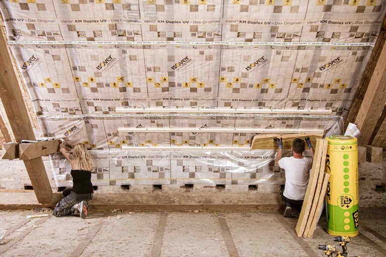 Izolarea mansardei cu vată izolatoare și folie de protecție împotriva vaporilor de către două persoane