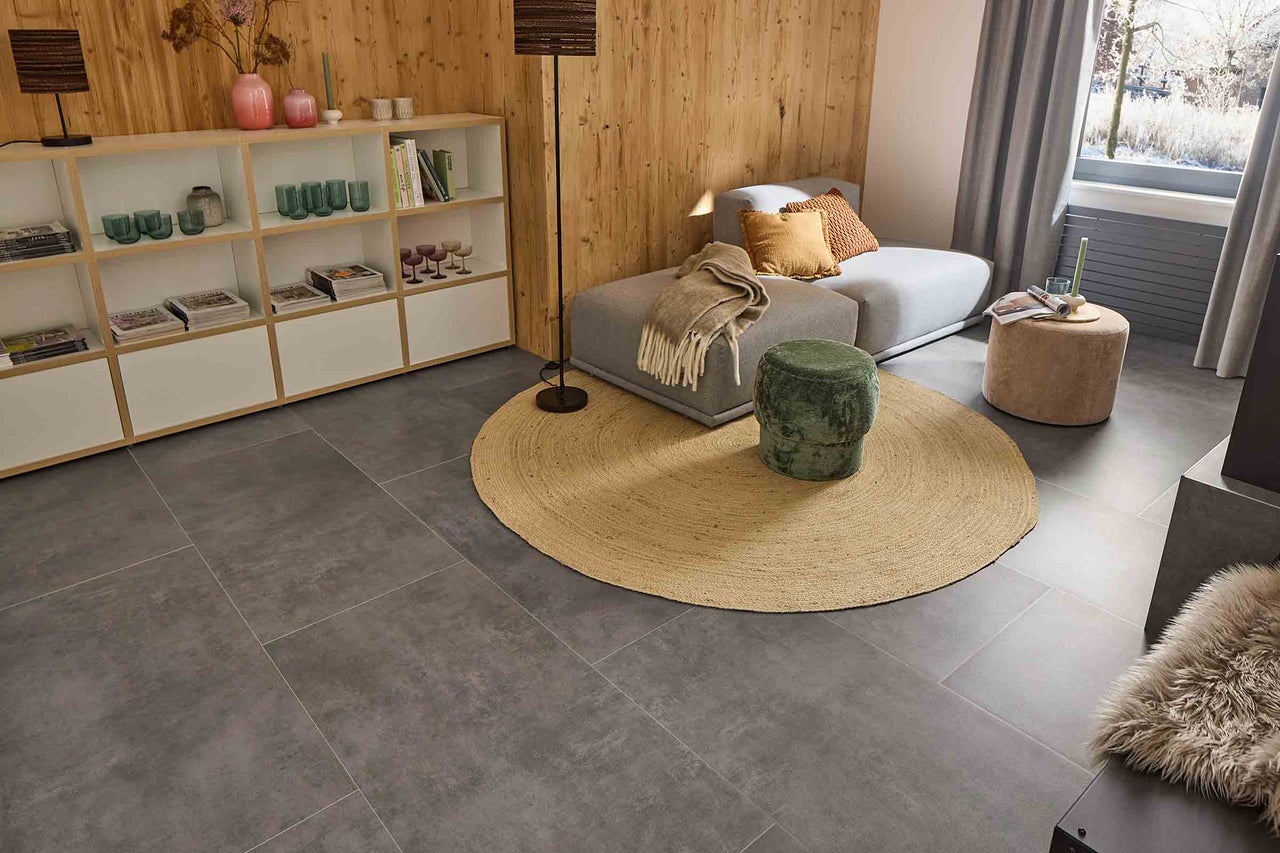 Living cu gresie gri, canapea, covor, taburet și raft.