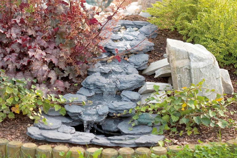 Peisaj decorativ de grădină cu pârâu din ardezie și plante înconjurătoare.