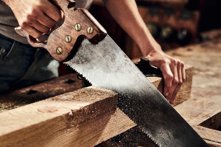 O persoană taie o bucată de lemn cu un ferăstrău manual.
