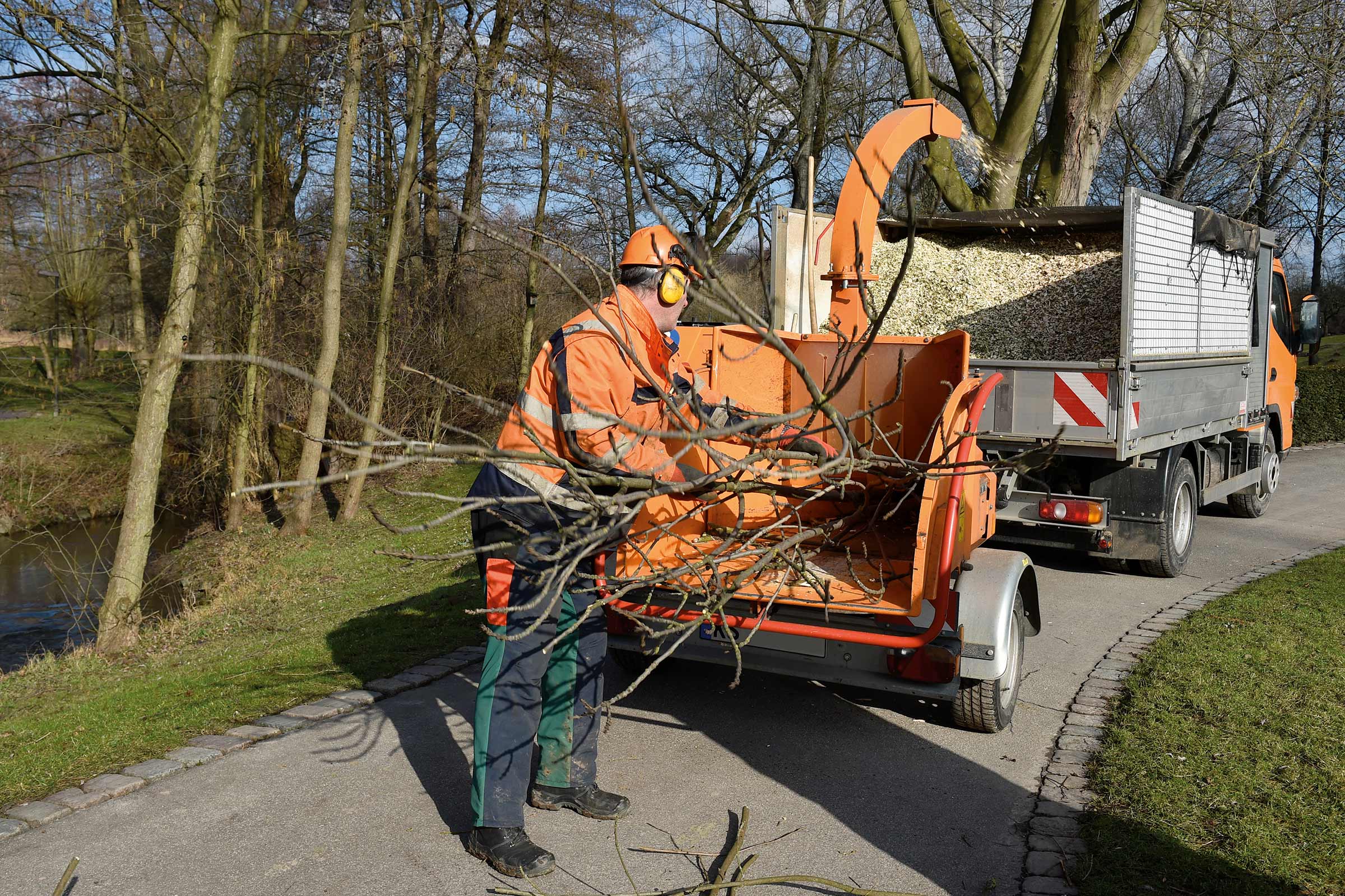 Un muncitor umple un tocător de lemn cu ramuri lângă un camion.