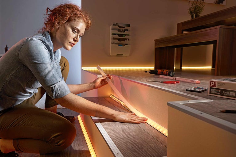 Femeie instalează benzi cu LED-uri pe o scară pentru iluminat ambiental