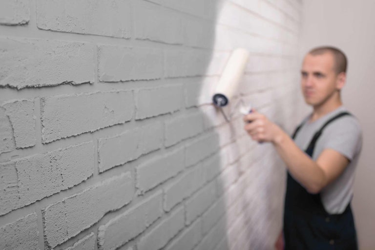 Un bărbat zugrăvește un zid de cărămidă cu trafaletul