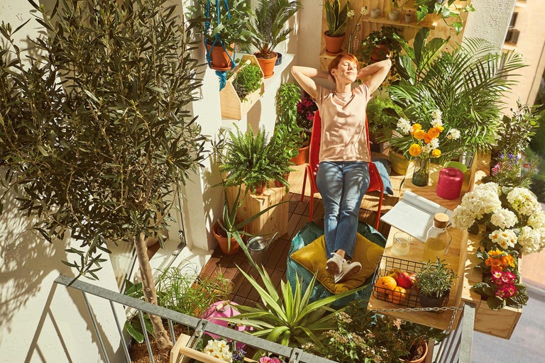Femeie relaxându-se pe un balcon verde cu plante în ghivece și jardiniere.