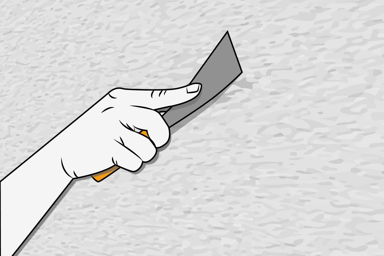O mână ține o spatulă în fața unui perete.