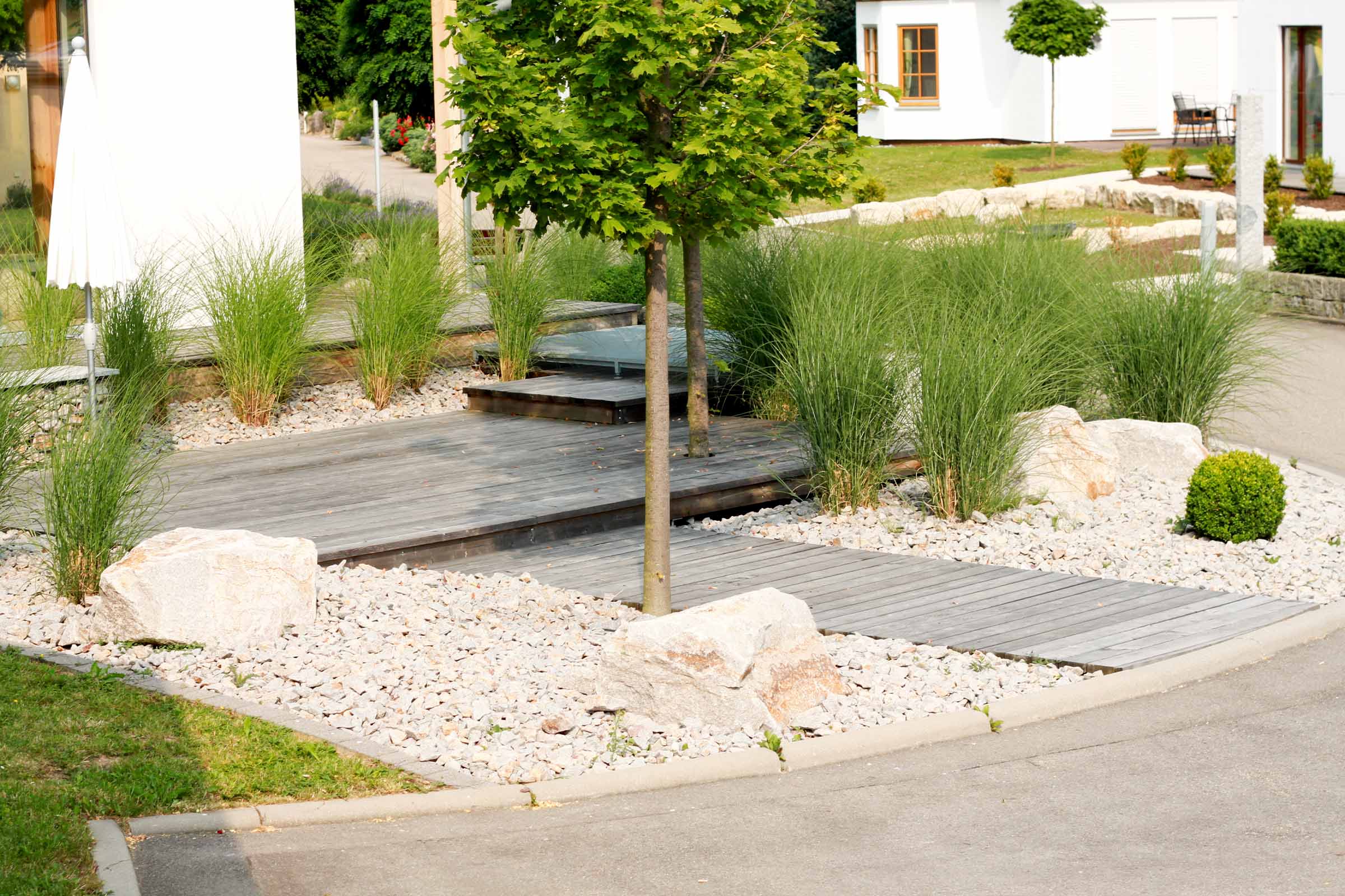 Grădină amenajată cu terasă din lemn, pietriș decorativ și plante