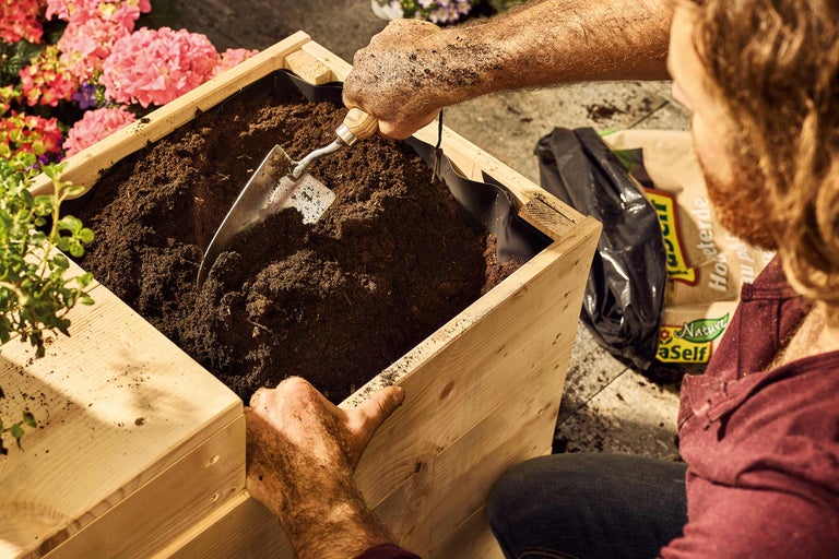 Persoană care umple un strat înălțat cu pământ de flori și o lopată mică.