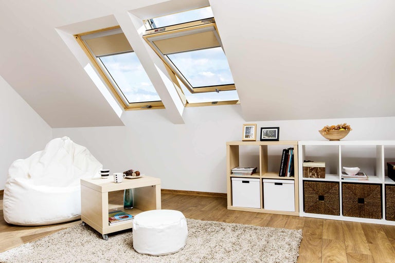 Cameră luminoasă de mansardă cu ferestre de mansardă și jaluzele, rafturi și mobilier de ședere.