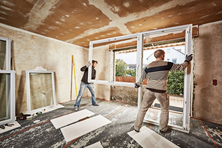 Doi meșteri montează o fereastră într-o cameră care are nevoie de renovare.