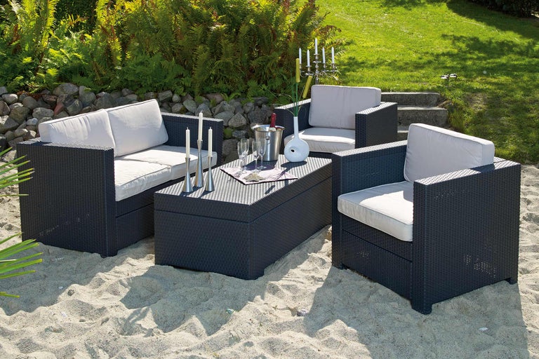 Set de mobilier de grădină cu două fotolii, o canapea și o masă pe o suprafață de nisip