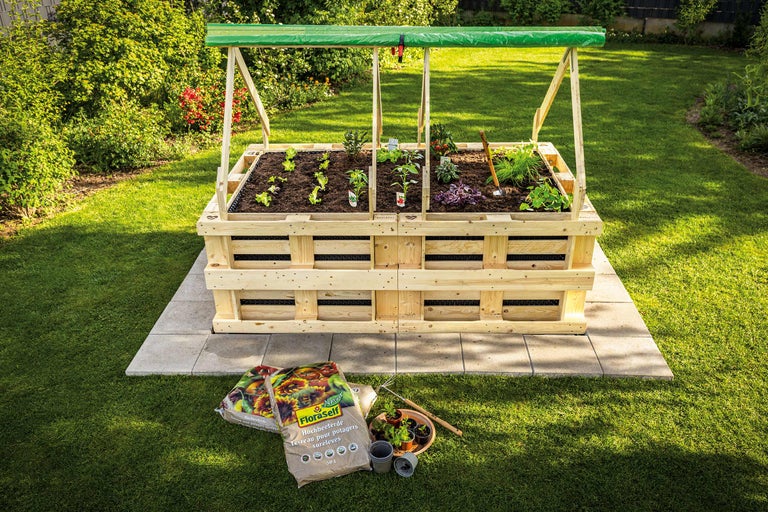 Jardiniere înălțată din lemn cu plante și legume în grădină, cu pământ de flori în prim-plan.