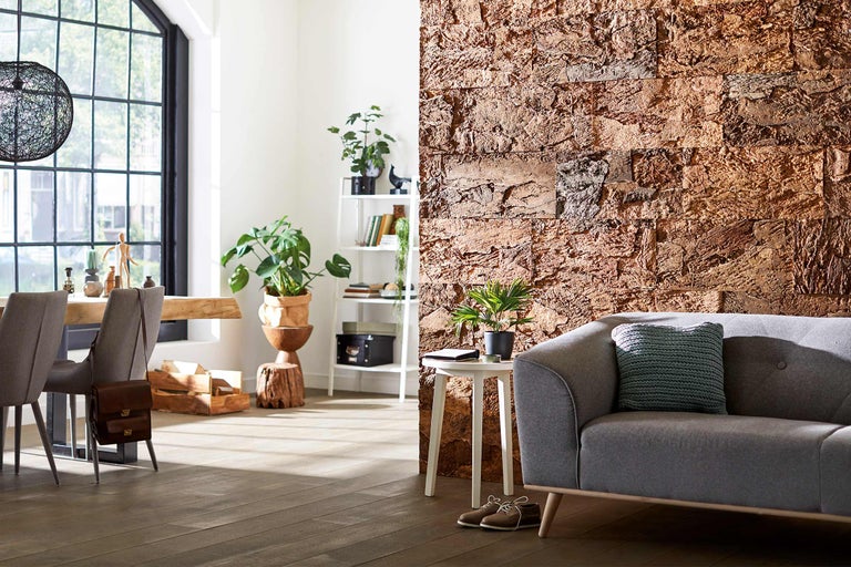 Cameră de zi luminoasă cu canapea, masă, plante și panouri de perete cu aspect de piatră