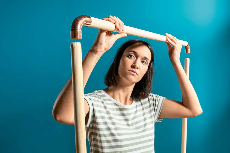 Femeie asamblând o structură tubulară cu fitinguri din lemn și cupru