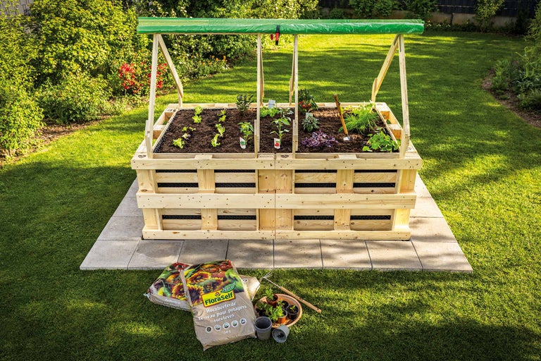 Jardinieră supraînălțată din paleți de lemn cu plante și pământ de grădină în grădină