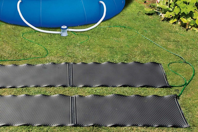 Două covoare solare de încălzire pe un gazon lângă o piscină cu pompă de filtrare.