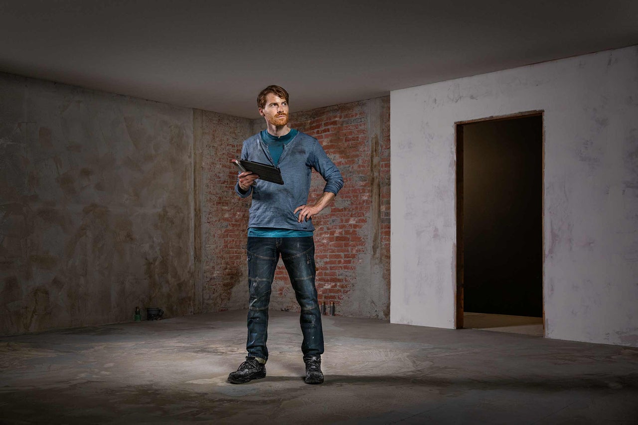 Mester cu tabletă într-o cameră care necesită renovare cu zidărie de cărămidă expusă