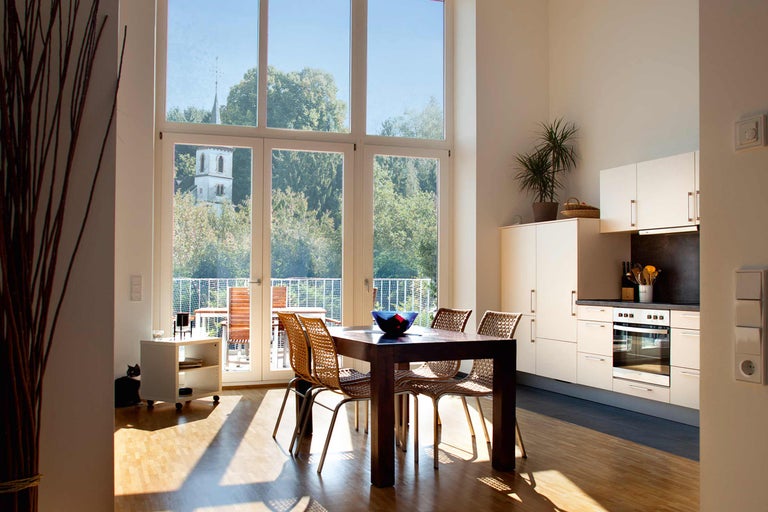 Zonă de luat masa luminoasă, cu masă din lemn, scaune, chicinetă și fereastră mare