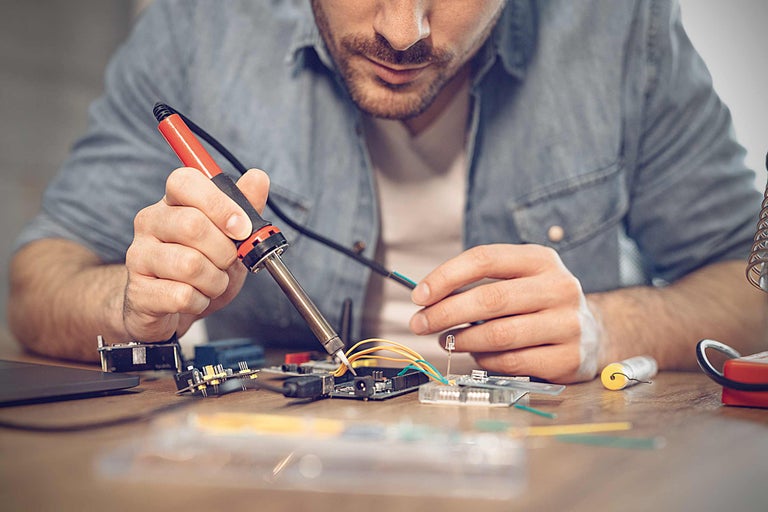Un bărbat sudează componente electronice cu un ciocan de lipit pe o placă de circuit imprimat.