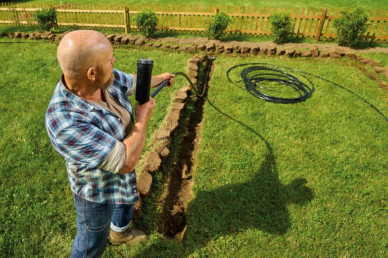 Un bărbat instalează un sistem de irigație într-o grădină
