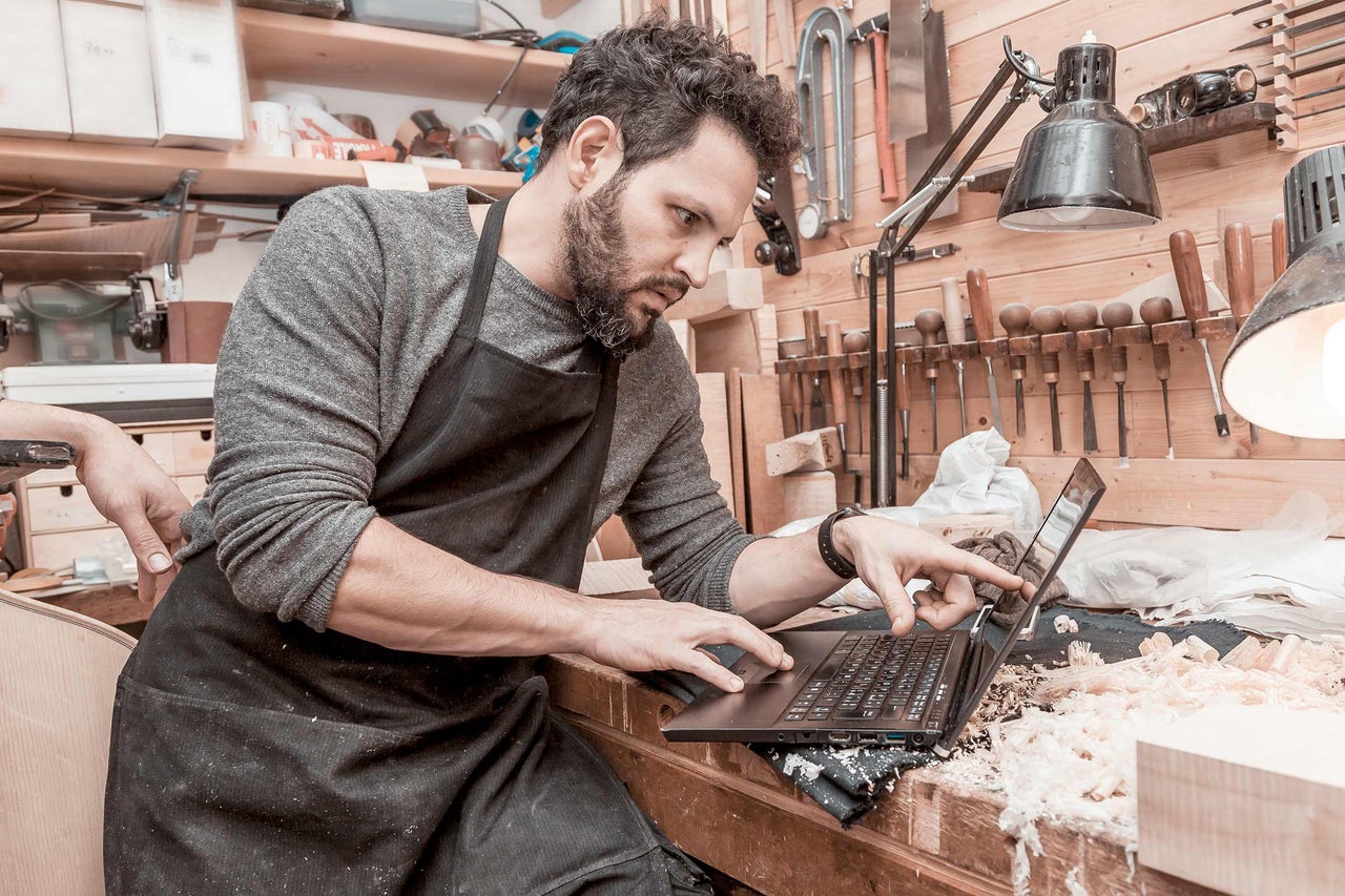 Un meșter cu șorț folosește un laptop într-un atelier.