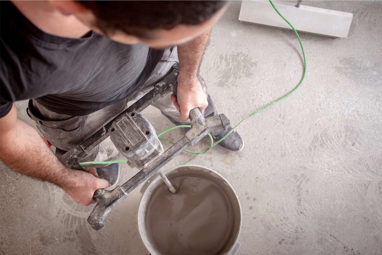 Artizanul amestecă mortar cu un mixer de mortar într-o găleată.