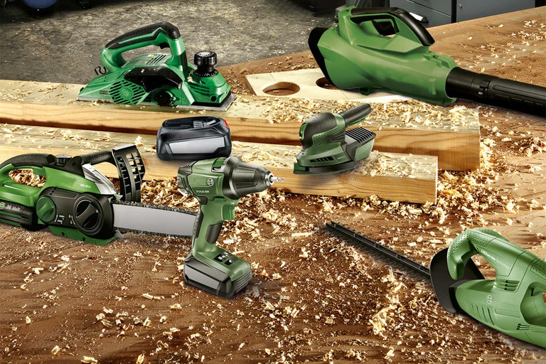 Set de scule de grădină cu acumulator, cu rindeluire, suflantă, drujbă, șurubelniță cu impact, șlefuitor și foarfece de gard viu pe o masă de lemn cu rumeguș
