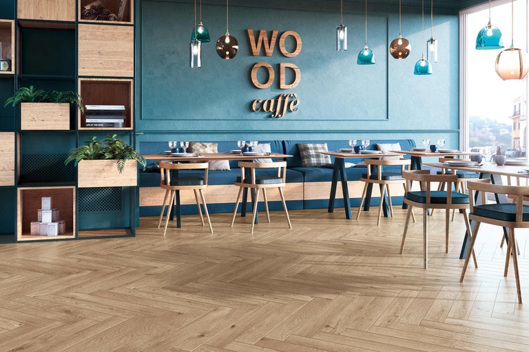 Fotografie de interior a unei cafenele cu mese, scaune și podea din lemn cu model herringbone.