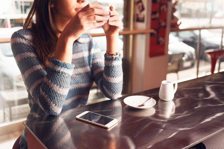 Femeie bea cafea într-o cafenea cu un smartphone pe masă