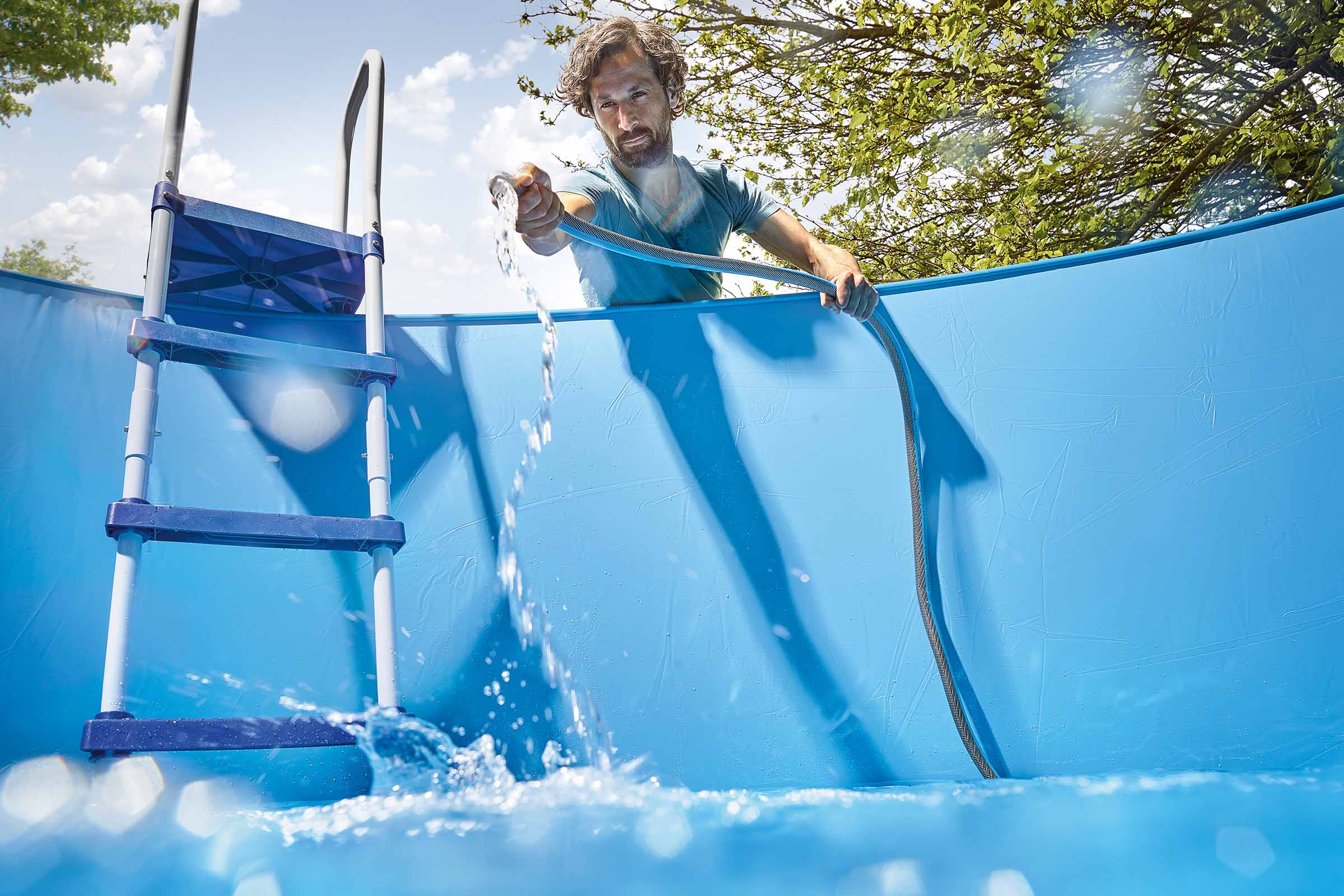 Bărbat umplând piscină cu furtun de apă; scară de piscină în imagine.