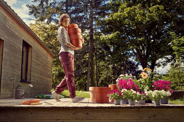 Femeie care poartă jardiniere în grădină pe o terasă din lemn