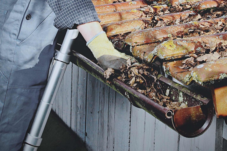 O persoană curăță o jgheabă de frunze și murdărie.