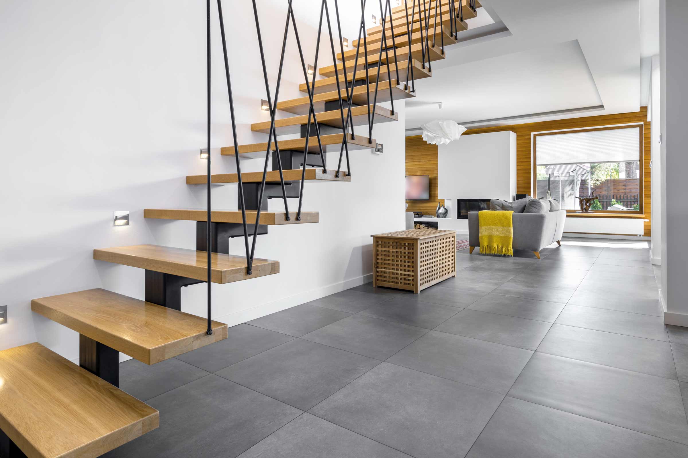 Cameră de zi luminoasă cu scară din lemn, gresie gri și mobilier modern
