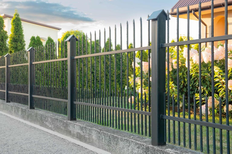 Gard metalic negru cu bare ascuțite și fundație de beton în jurul unei proprietăți.