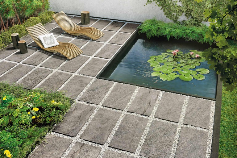 Scenă de grădină cu plăci de terasă, rosturi cu pietriș, iaz, șezlonguri și plante