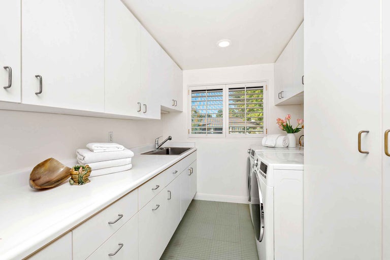 Spălătorie luminoasă cu mașină de spălat, uscător, chiuvetă și dulapuri albe