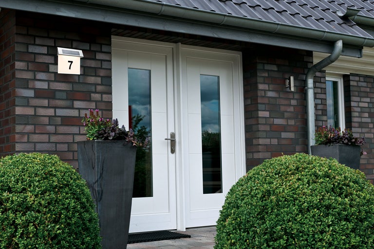 Intrarea unei case cu ușă dublă, număr de casă iluminat și vegetație